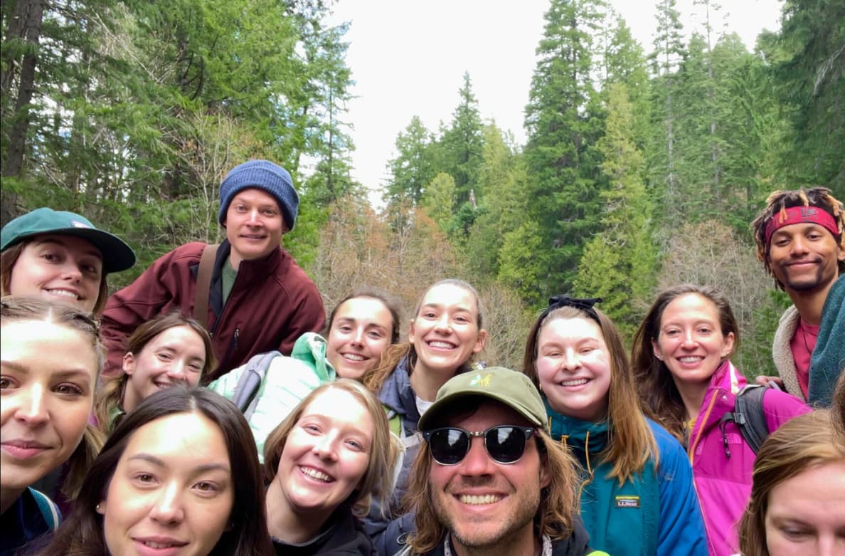 Group of hikers outdoors in a forest, smiling for a selfie.