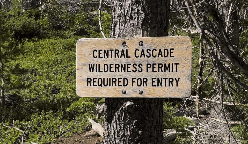 Wooden sign on tree reading 'Central Cascade Wilderness Permit Required for Entry' in forest setting.