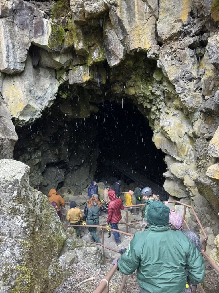 Group of adventurers entering a rocky cave with water dripping, wearing helmets and jackets.