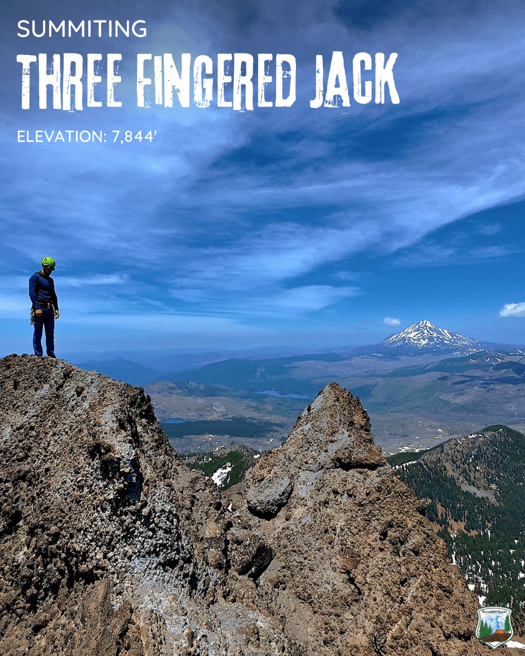 Hiker on rocky summit with snow-capped mountain view under blue sky